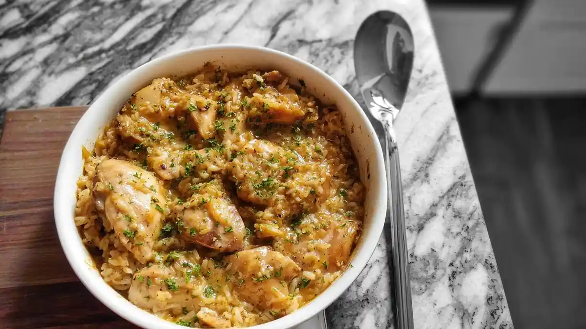 creamy one-pot chicken and rice dish with parsley garnish served in a white bowl on marble surface