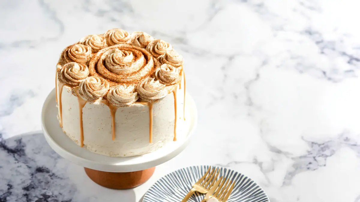 cinnamon spiced cake with rosette frosting and caramel drip on marble cake stand
