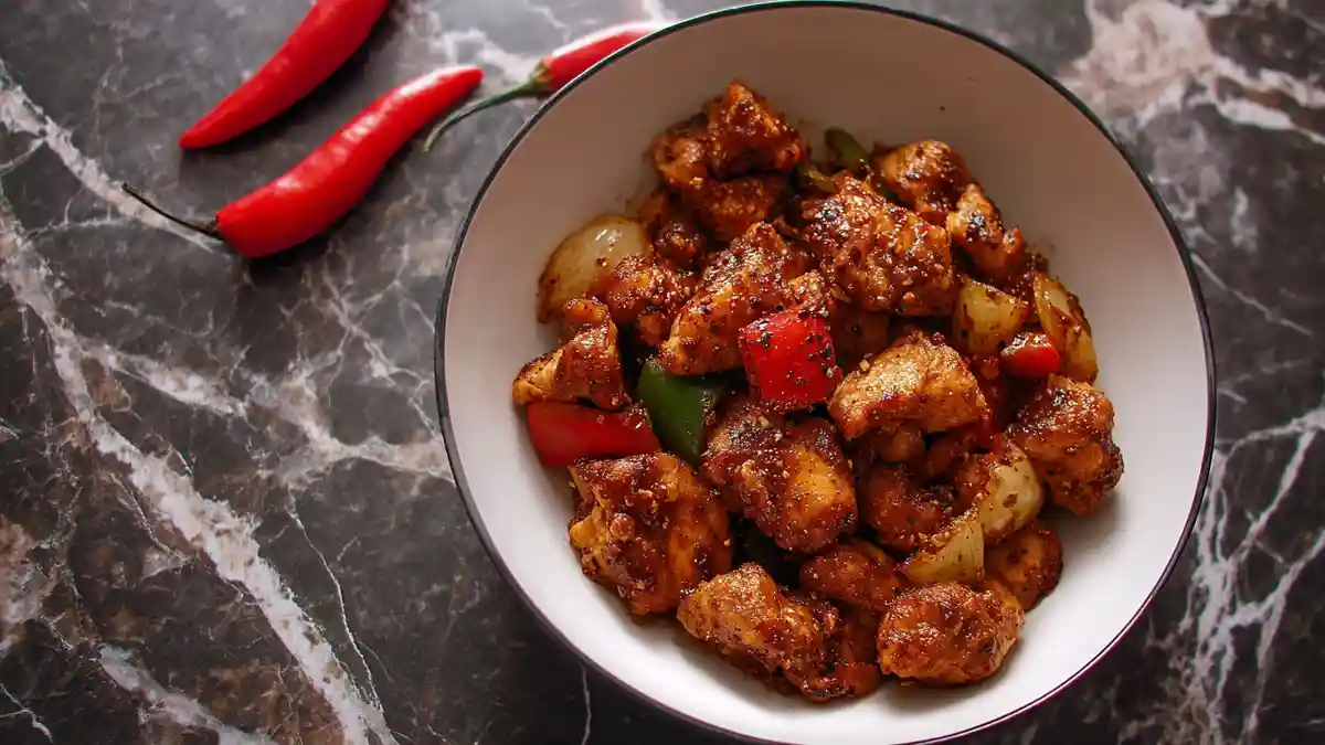 Bowl of spicy pepper chicken with bell peppers and onions on a marble background