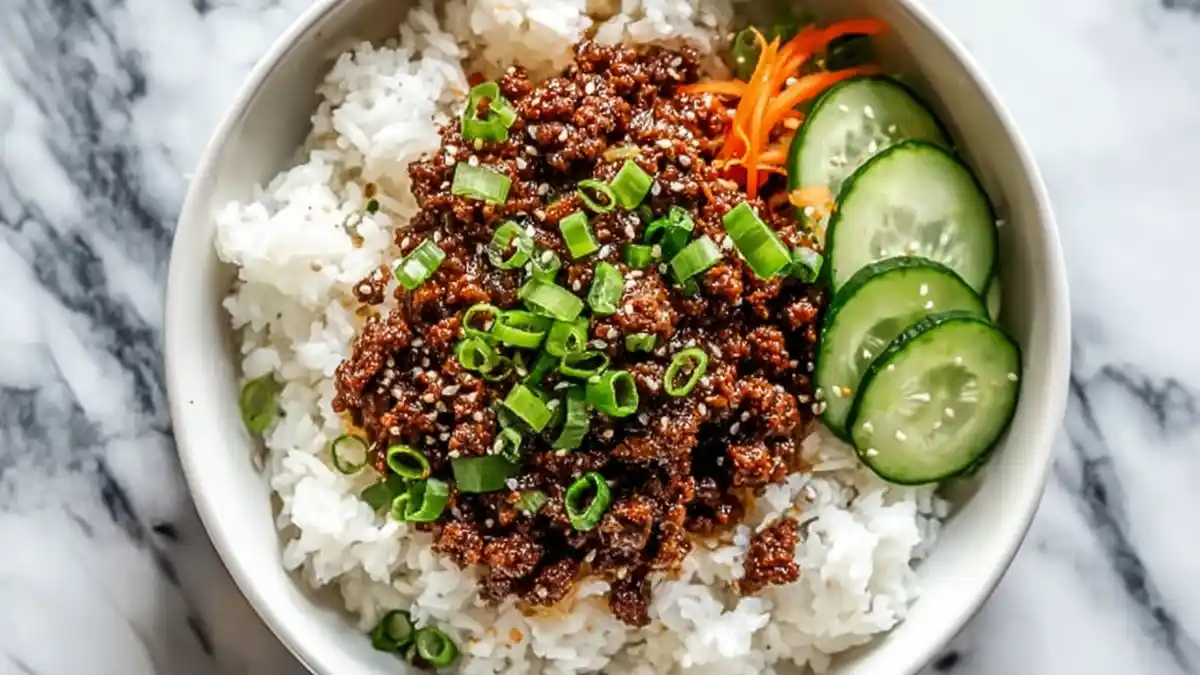 korean ground beef rice bowl with white rice, cucumber slices, shredded carrots, and scallions