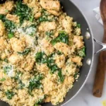 skillet with quinoa, chicken pieces, spinach, and grated parmesan