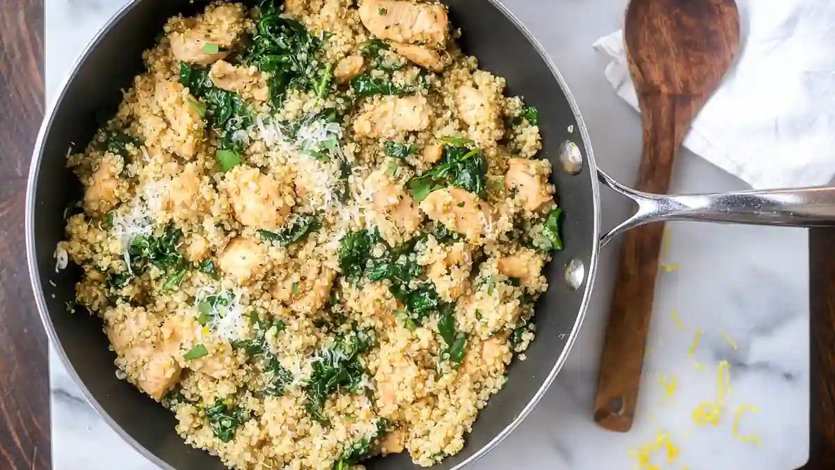 skillet with quinoa, chicken pieces, spinach, and grated parmesan