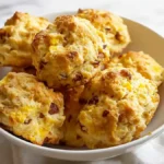 golden cheddar bacon biscuits stacked in a white bowl on a white napkin